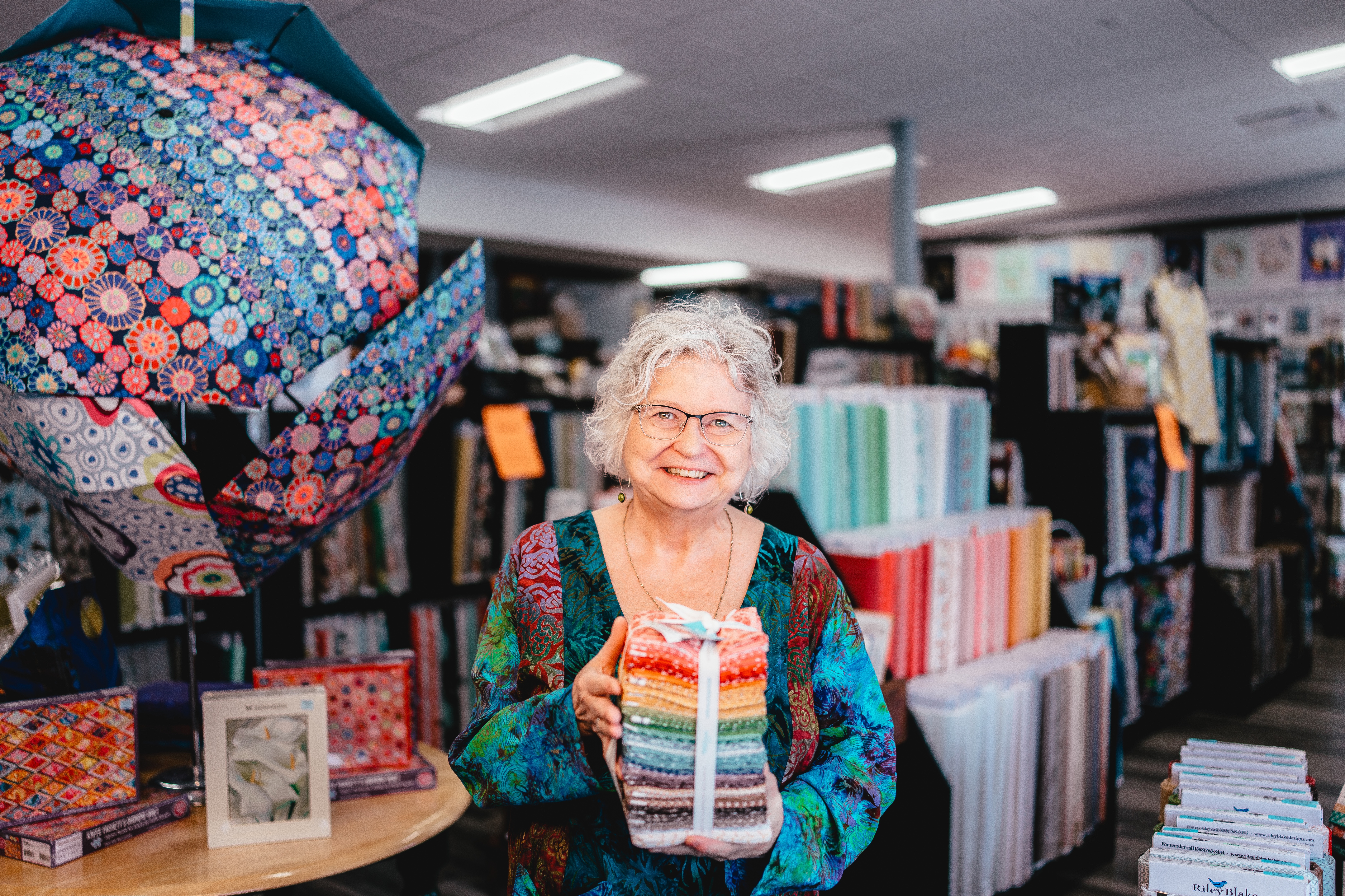 Cherished Pieces shop owner smiles among the bright colours of the quilt materials and supplies