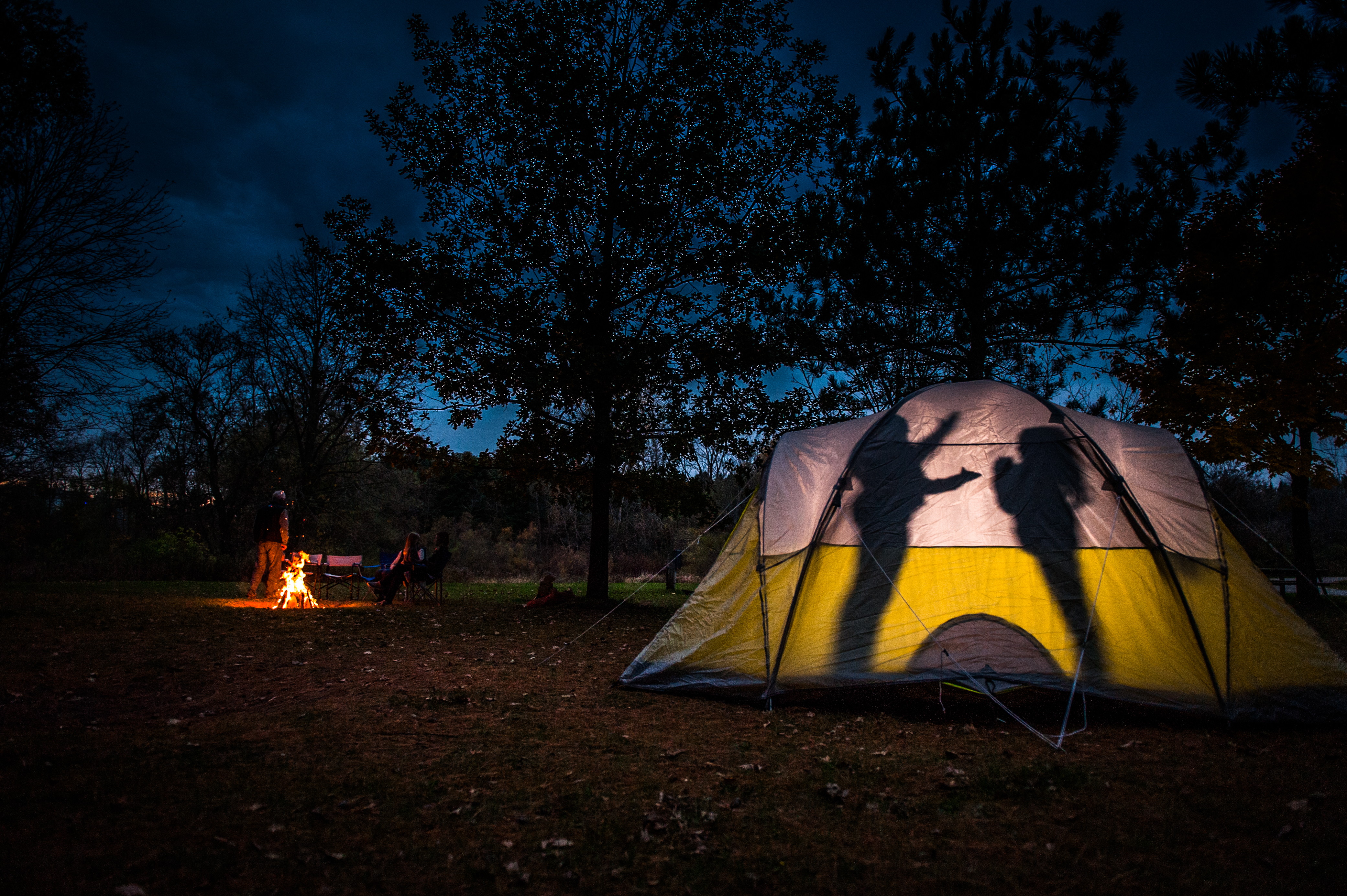 two people having a fire while kids make shadow puppets in their tent