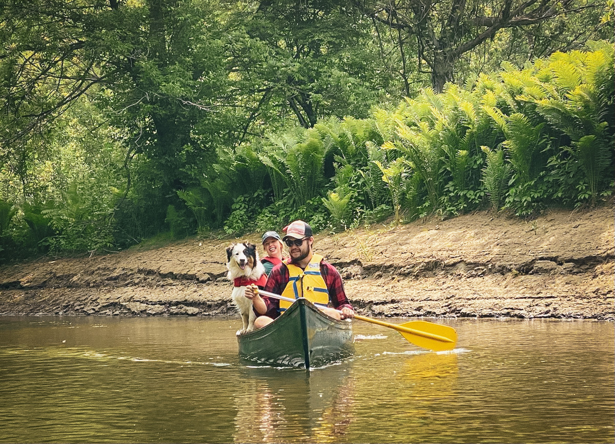 An aussie dog smiling, in a canoe with owners paddling