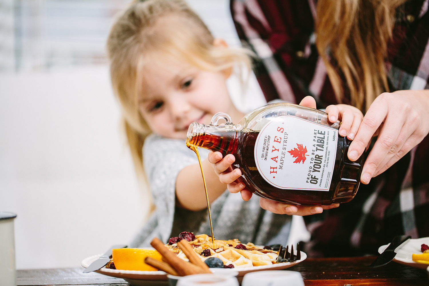 little girl pouring maple syrup over her waffles