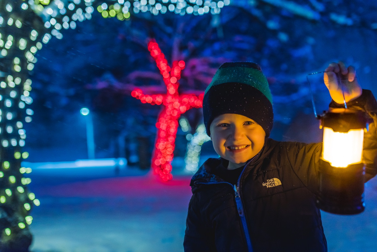 child holding lantern in front of night time winter light display in ingersoll